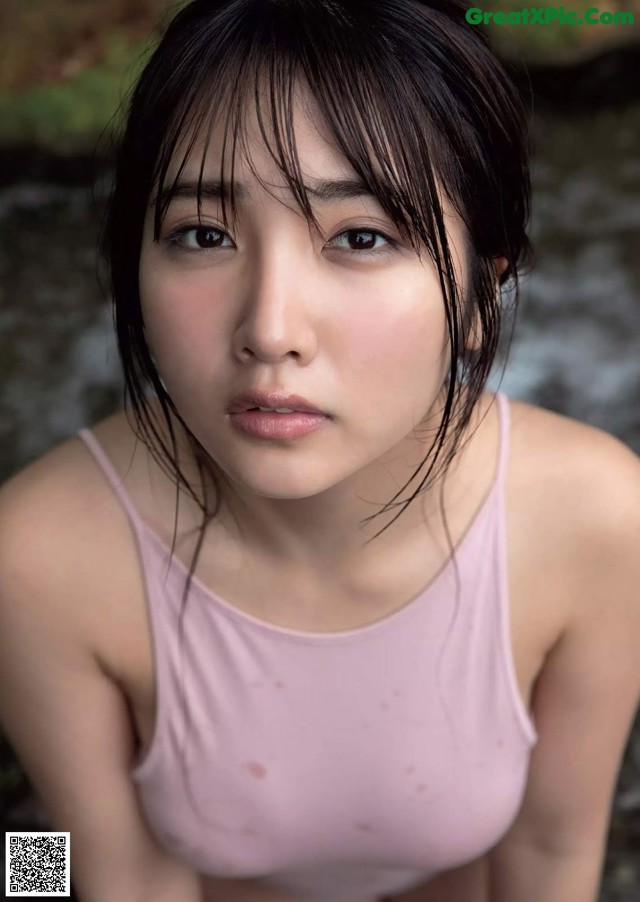 A woman in a pink tank top sitting on a rock.